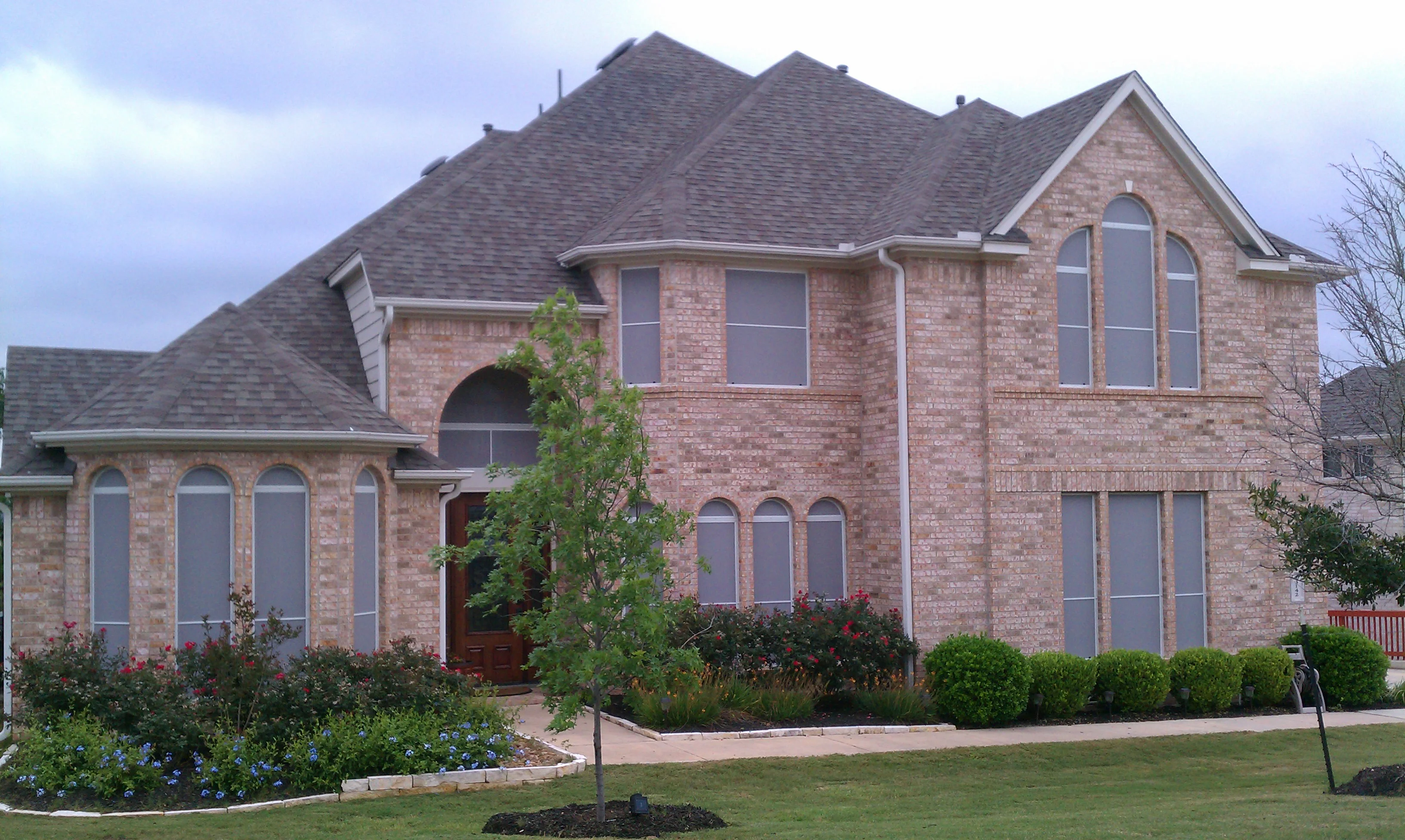 Solar screens installed on multi-story brick home with arched and picture windows