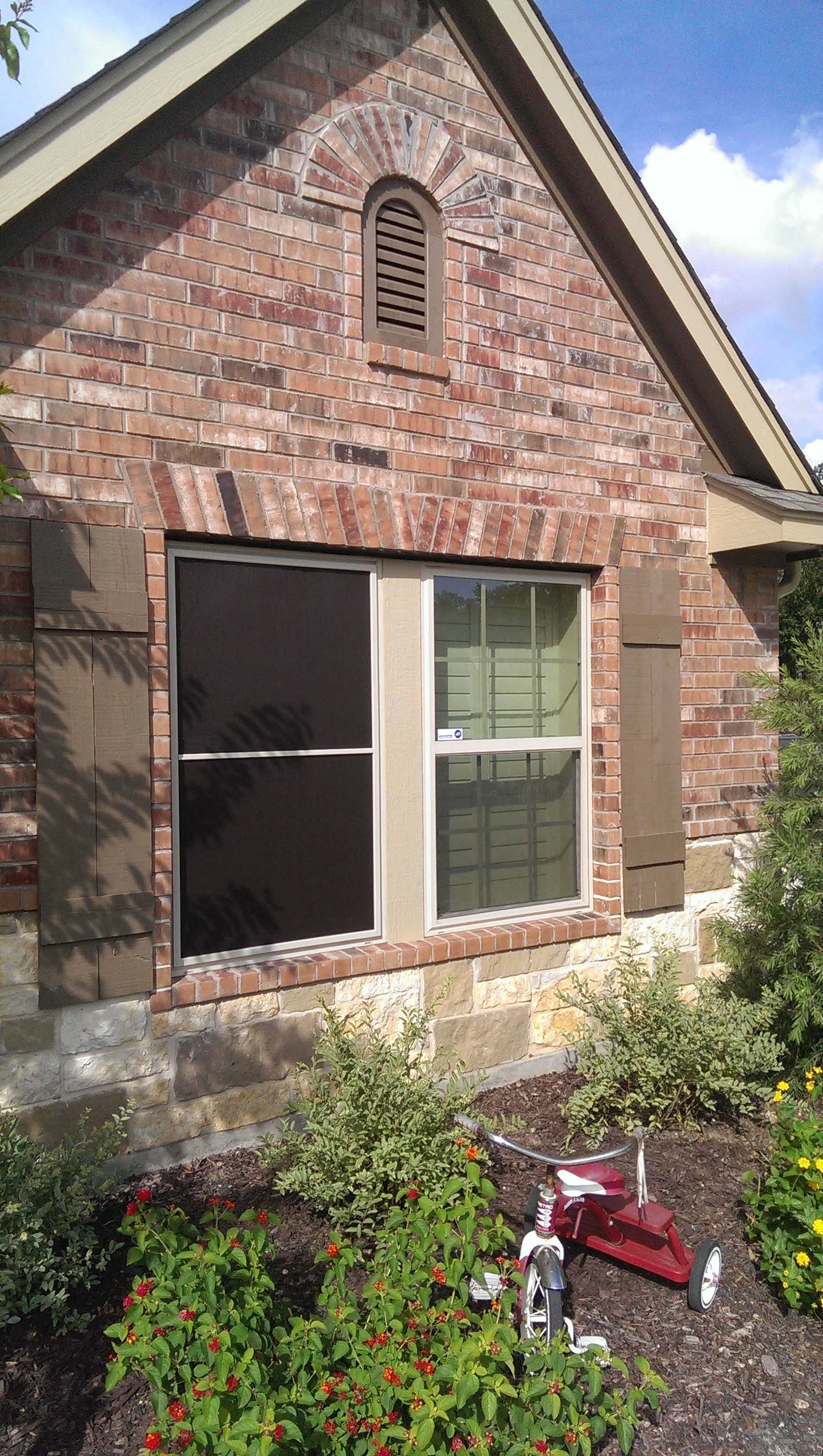 Black solar screens installed on brick home window with white trim and decorative brick detailing