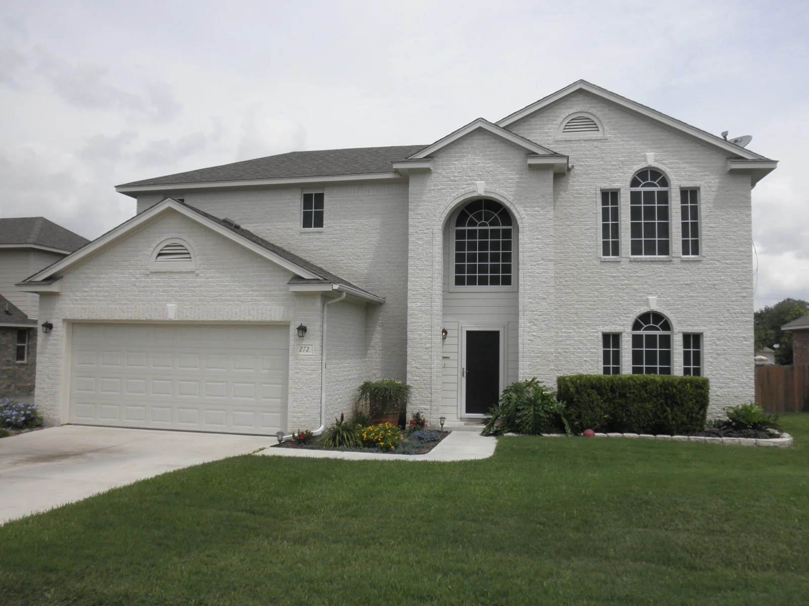 Two-story white brick home with arched and rectangular windows, white trim, and garage door