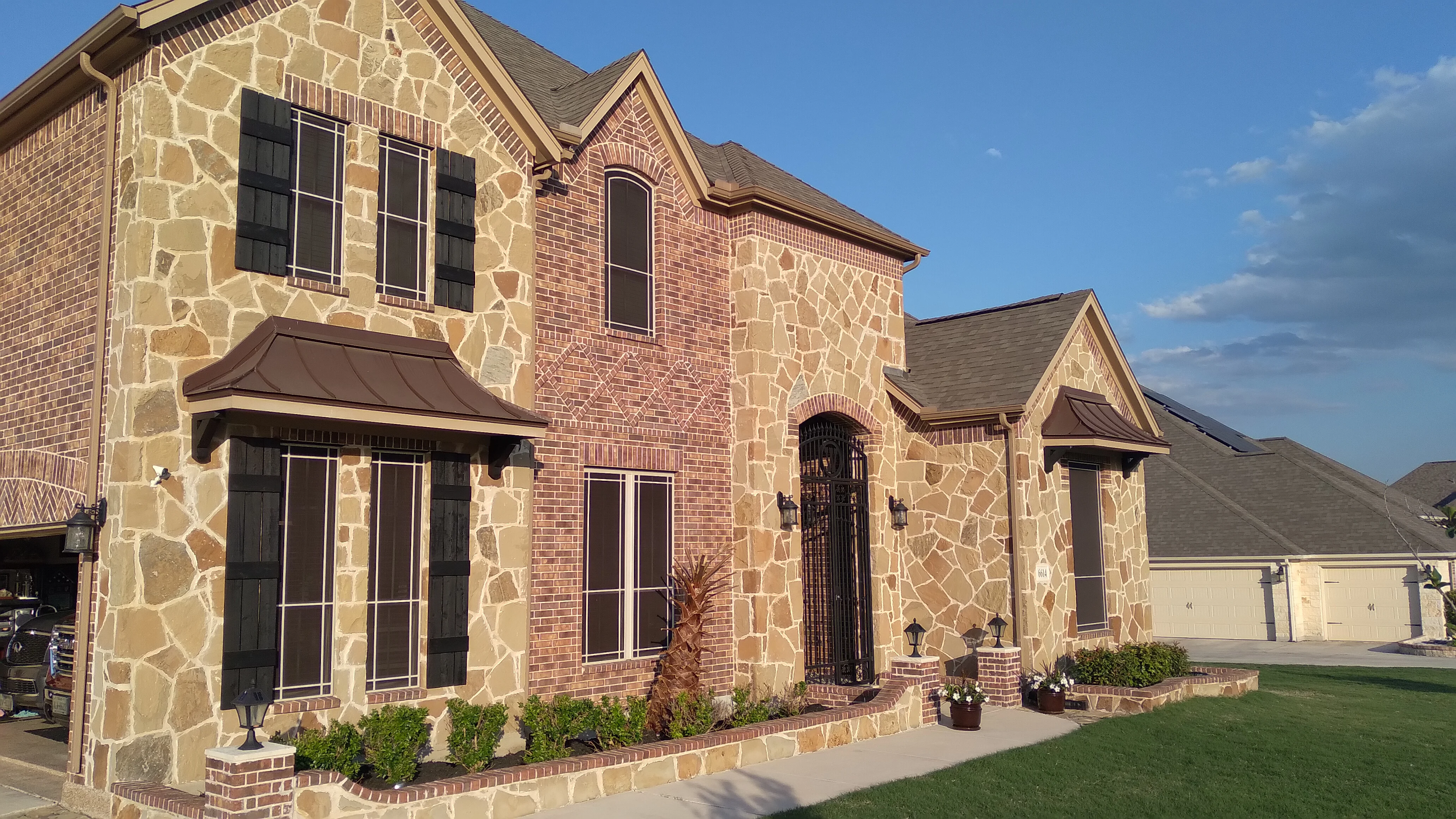Stone and brick home with black solar screen windows installed on front facade
