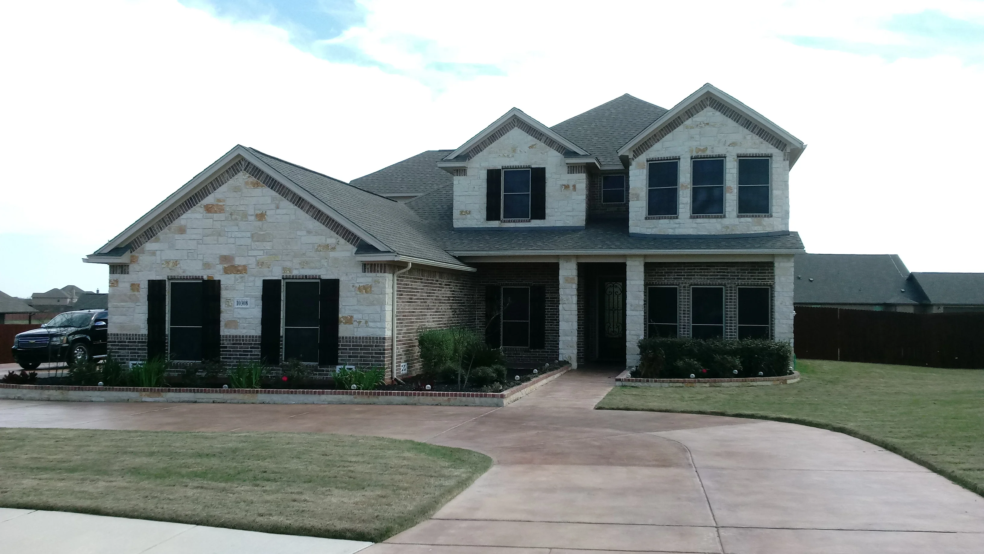 Two-story home with black-framed window installations on white stone and brick exterior