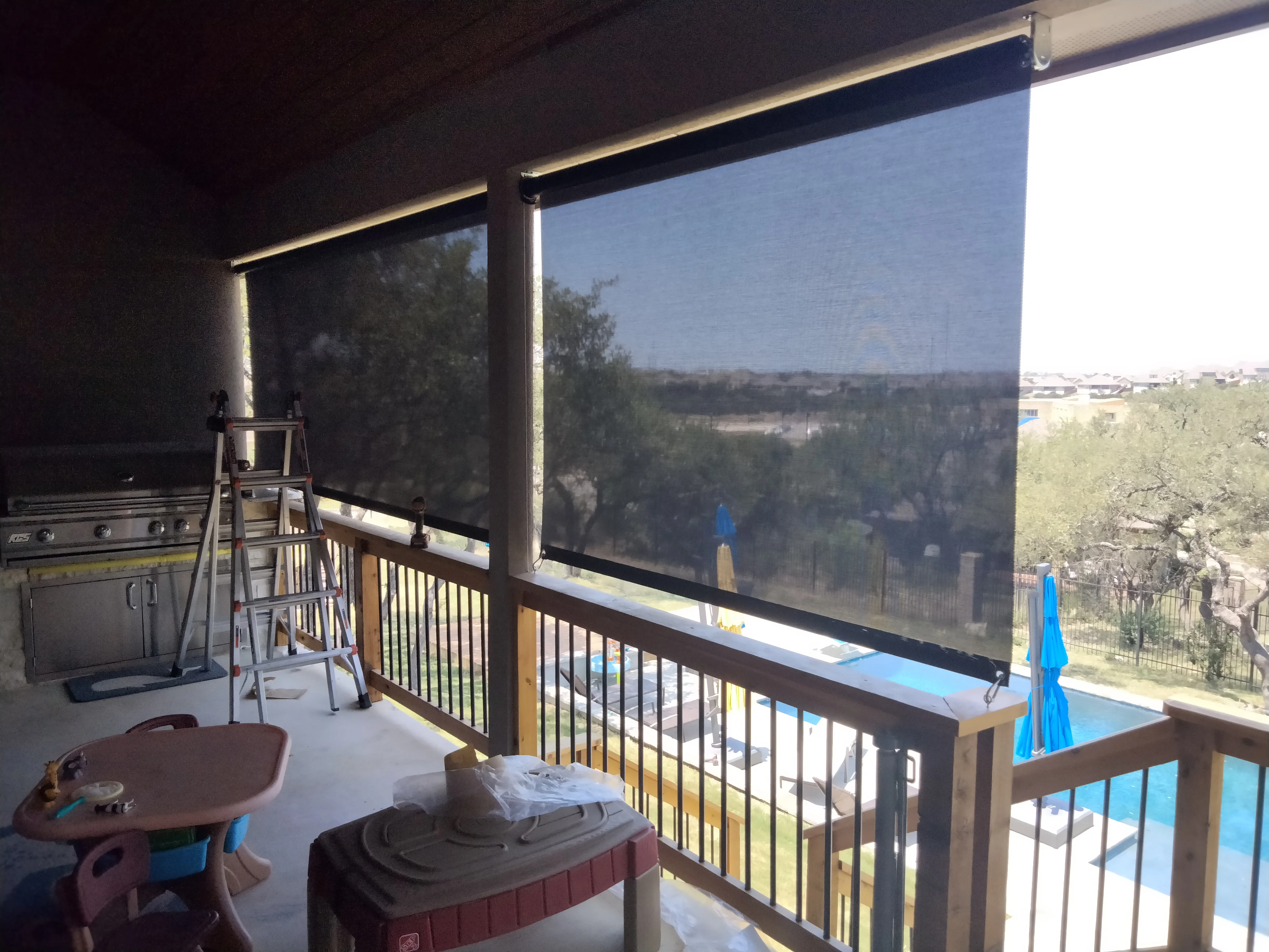 Motorized retractable solar screen with dark mesh on deck railing, aluminum frame with LED lighting