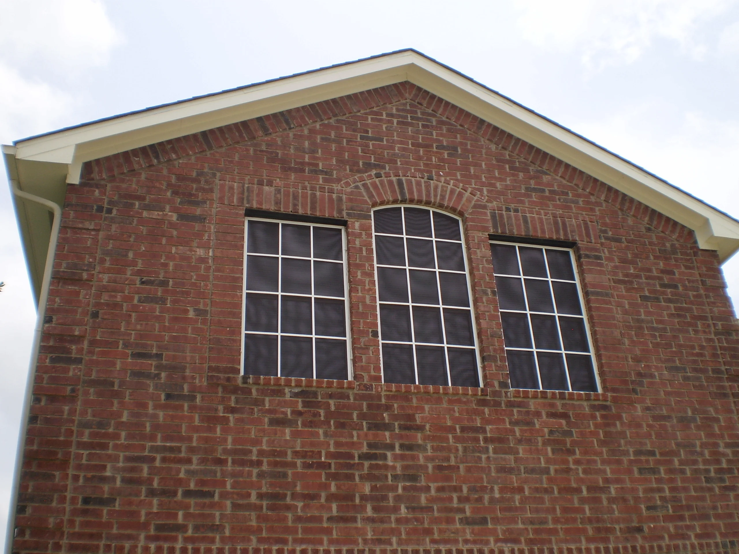 Three white grid windows installed in red brick gable wall with white trim
