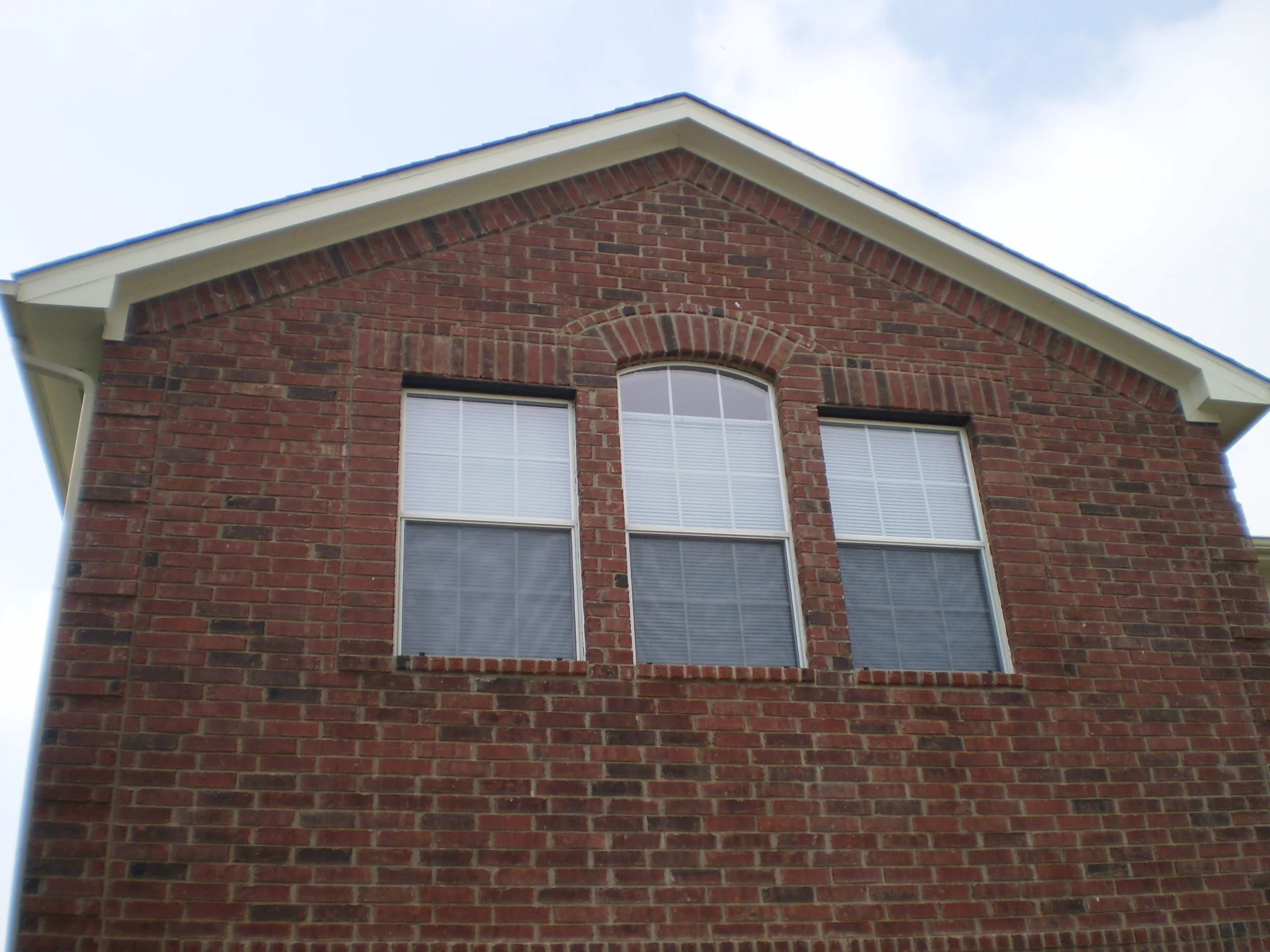 Three white double-hung windows with blinds installed on red brick home facade