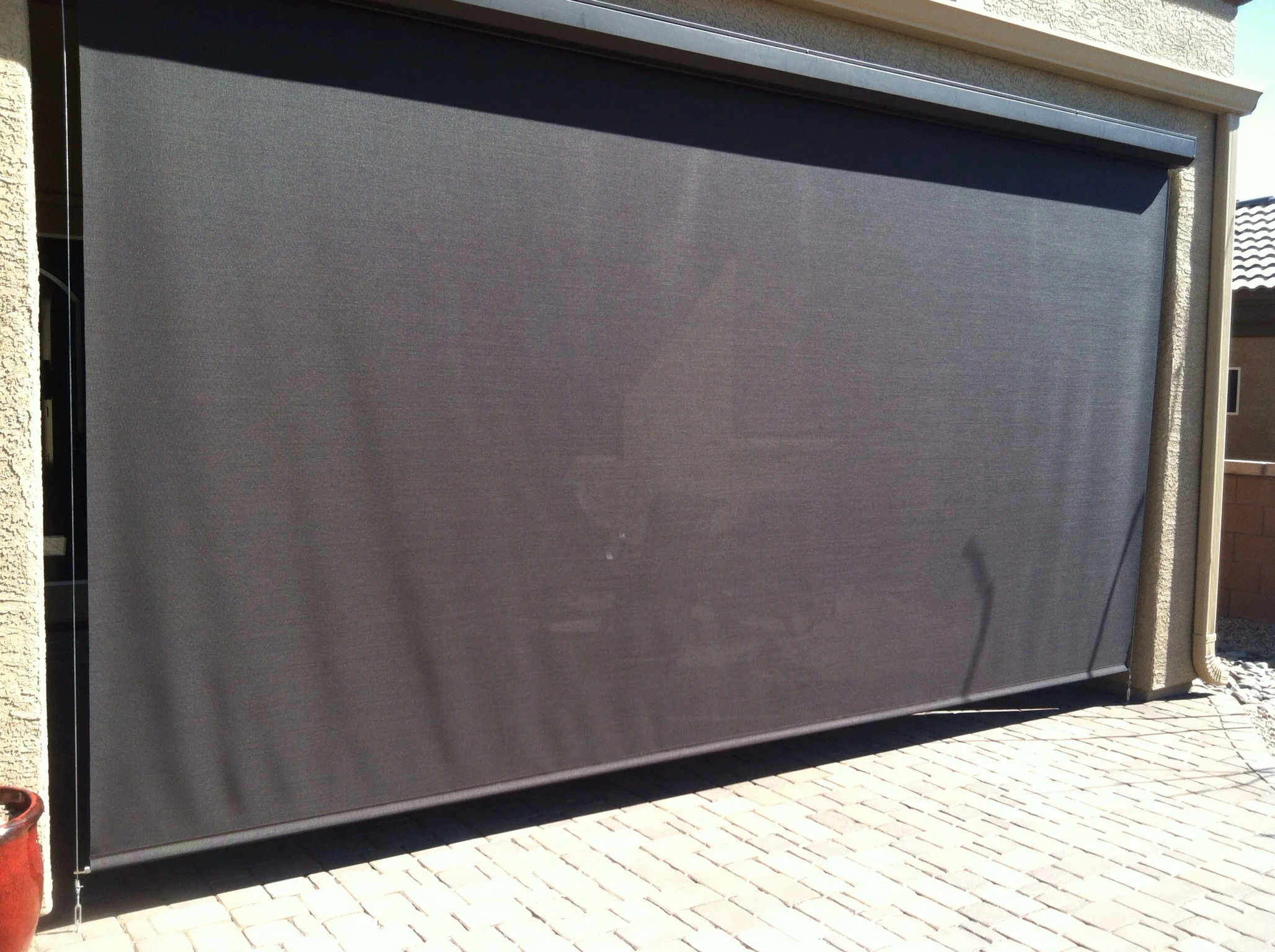 Motorized retractable solar screen with gray mesh fabric and aluminum frame on garage opening