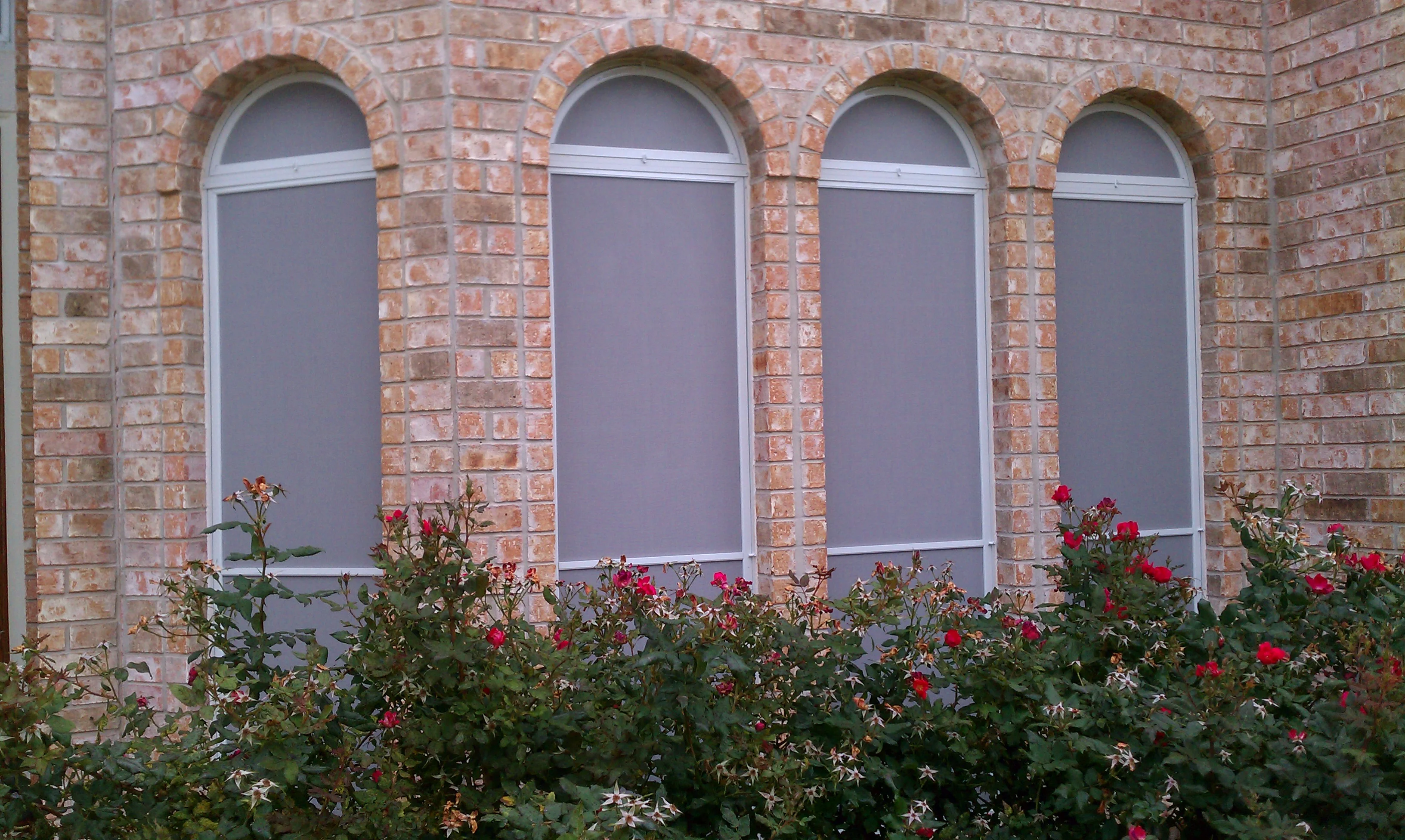 Four arched windows with white-framed solar screens on red brick wall