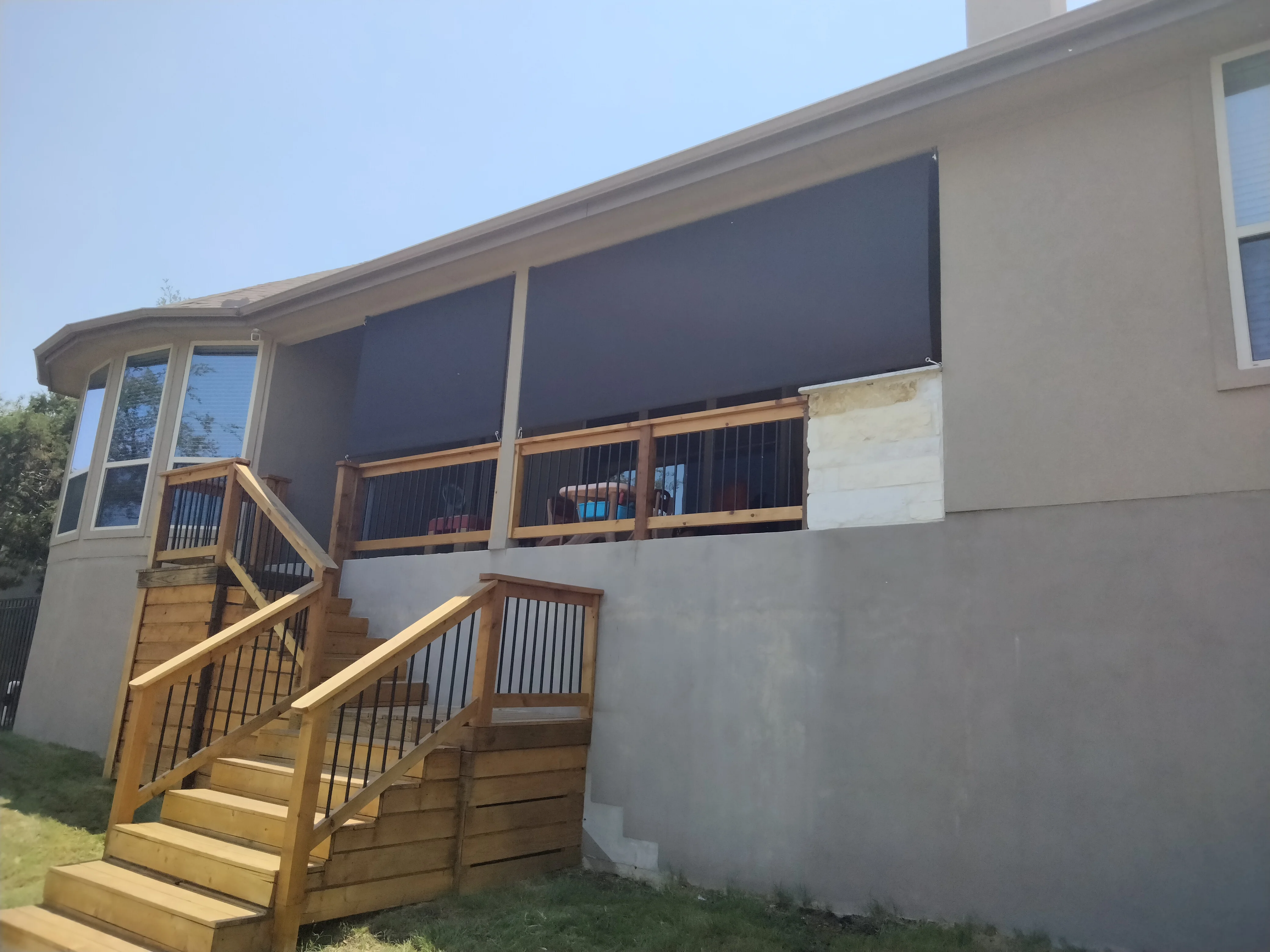 Retractable dark solar screens installed on multi-panel windows with wooden deck railings and metal balusters