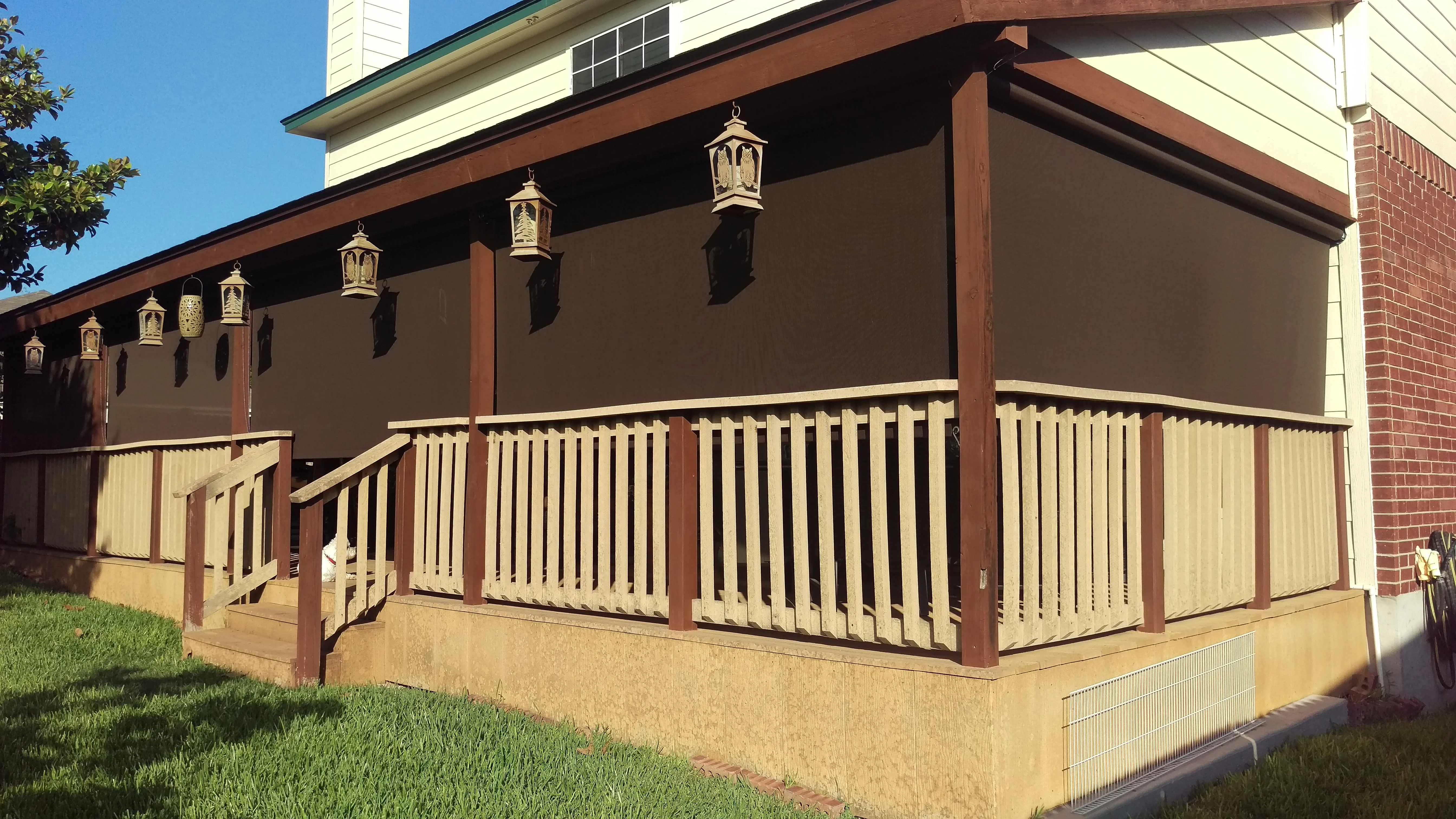 Brown solar screen patio enclosure with wood frame, cream balusters, and brass lantern fixtures