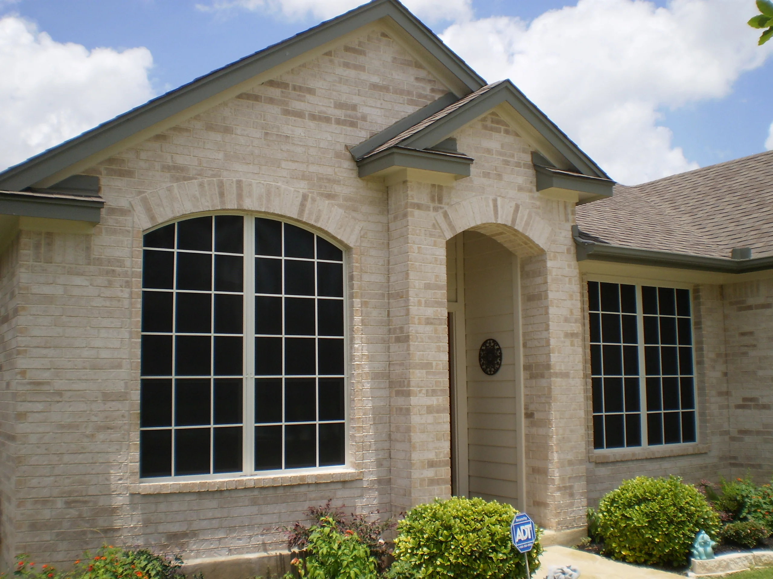 Large arched grid windows with white frames installed on tan brick home exterior