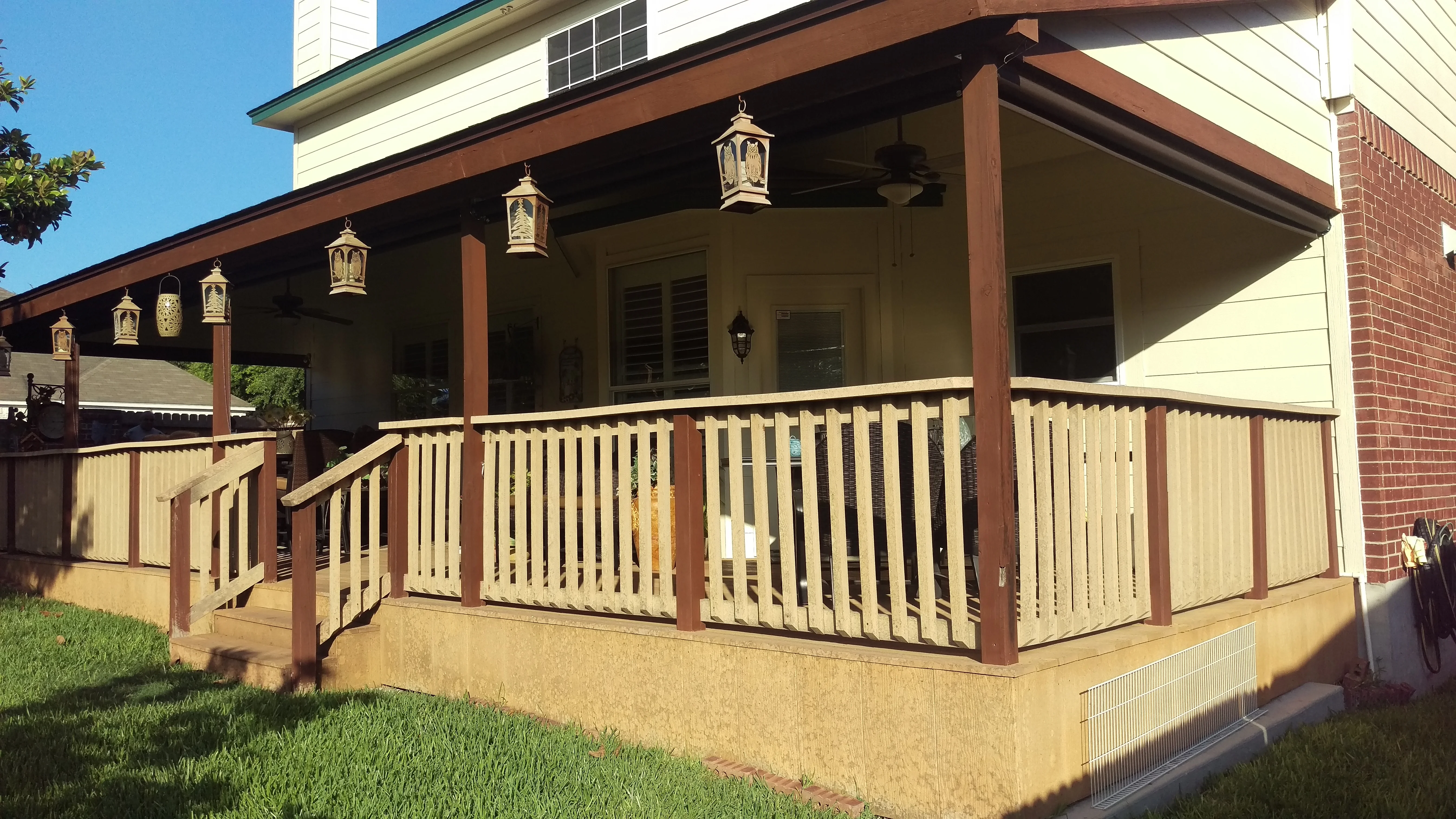 Covered porch with brown posts, cream balusters, and solar screening on residential home