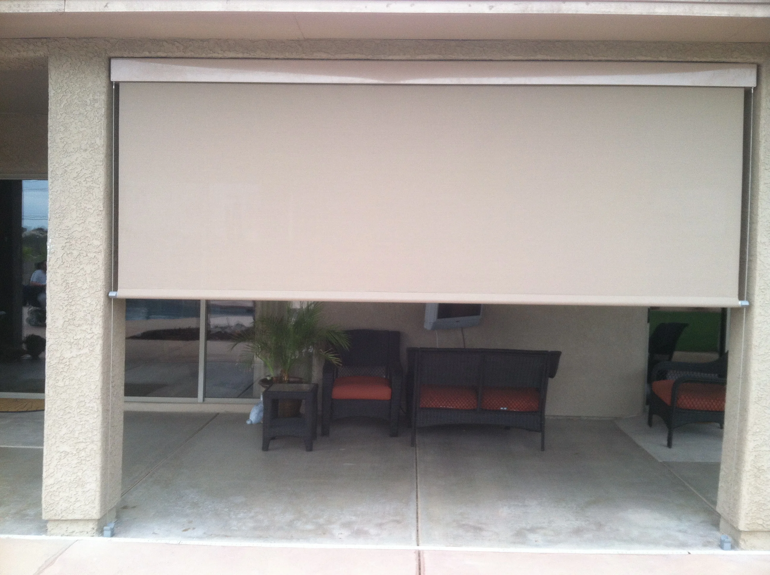 White exterior roller shade with aluminum frame and cable system over patio seating area