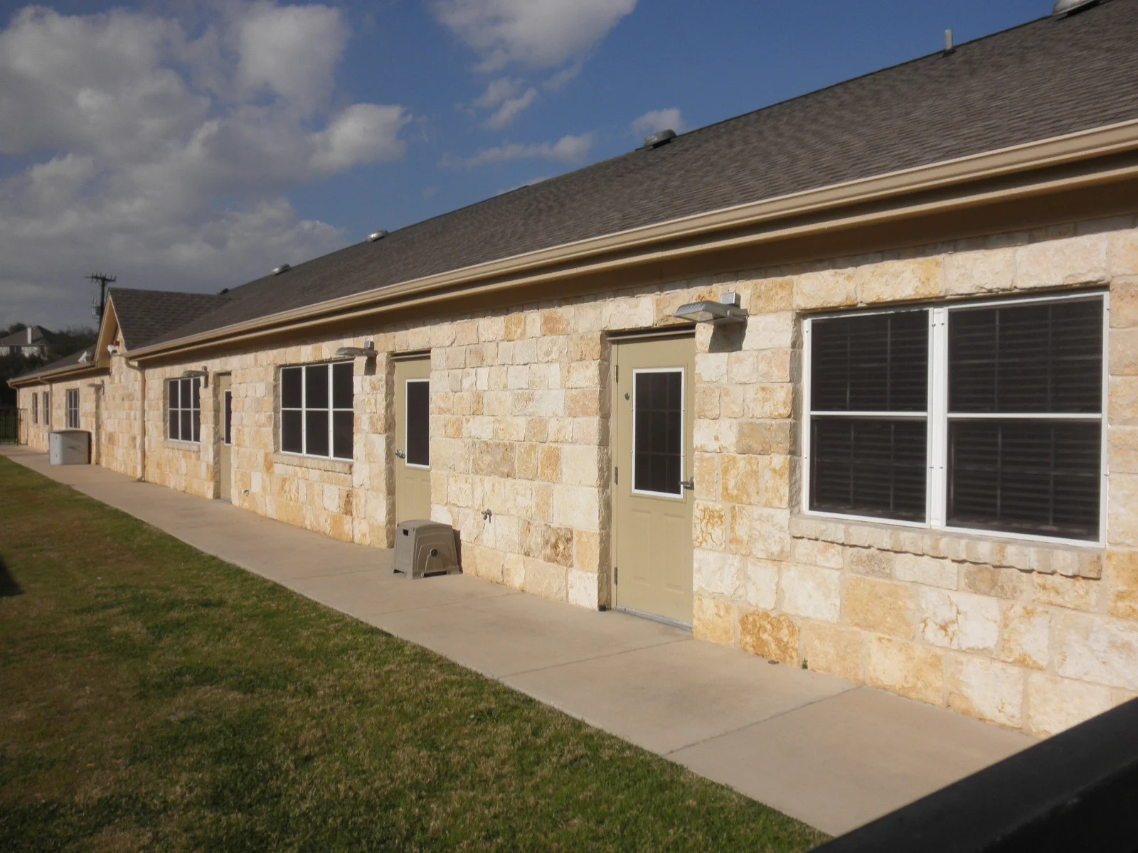 Black solar screens installed on stone building windows with tan trim and concrete walkway