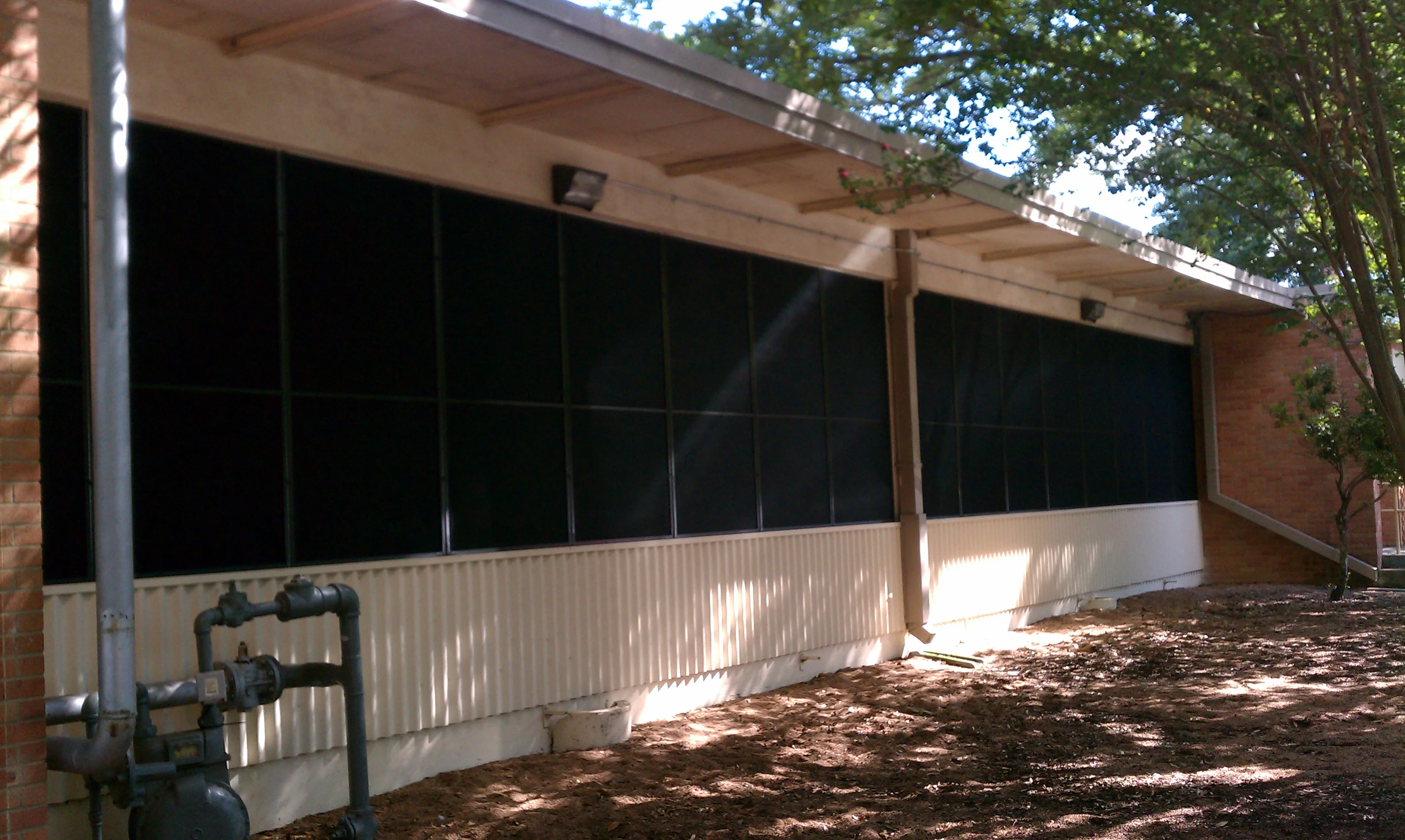Black solar screens installed on large institutional windows with metal wainscoting and wooden patio structure