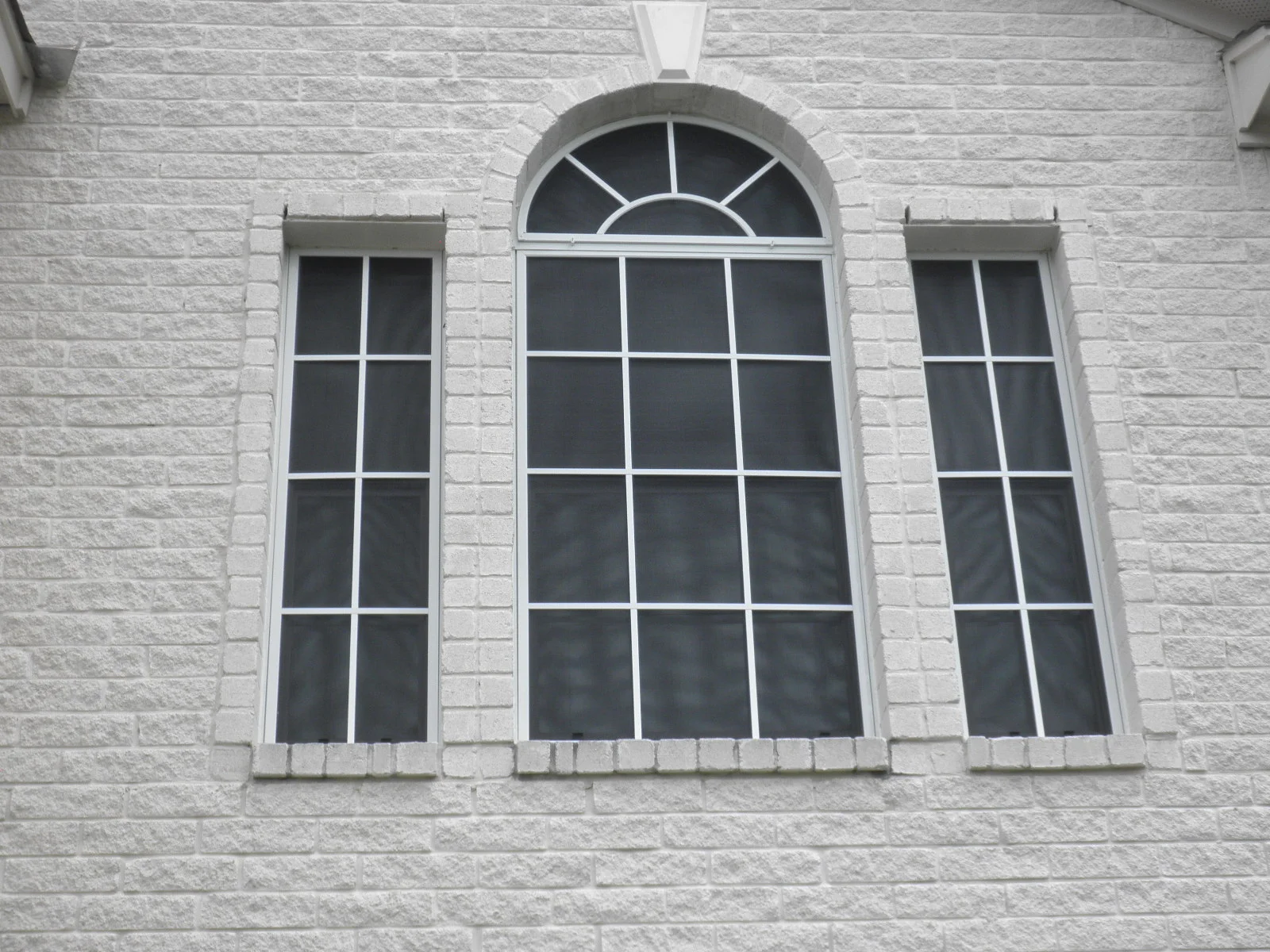 Three tall multi-pane windows with white frames and arched transom on brick wall