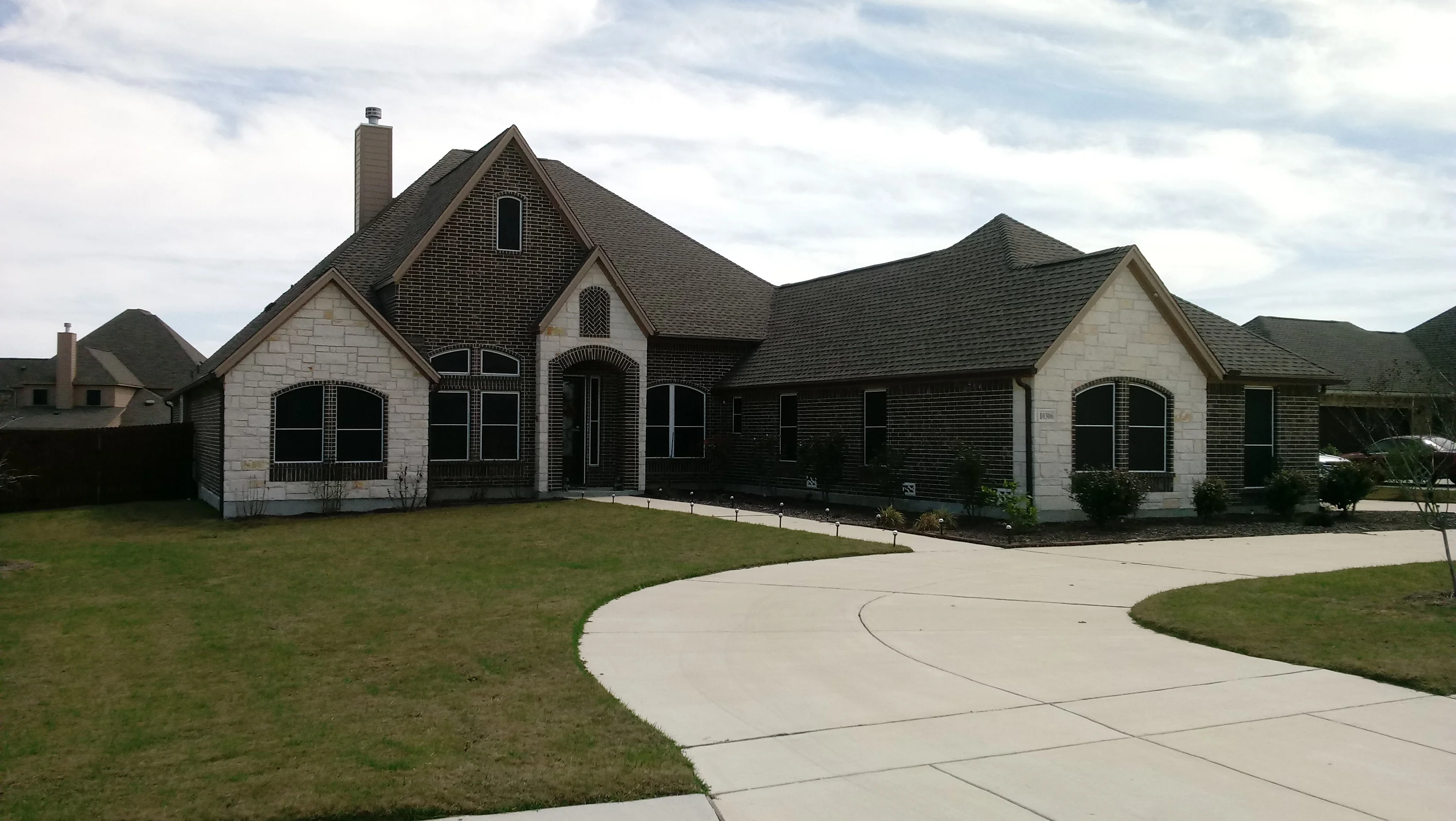 Two-story home with arched windows, brick and stone exterior, curved driveway