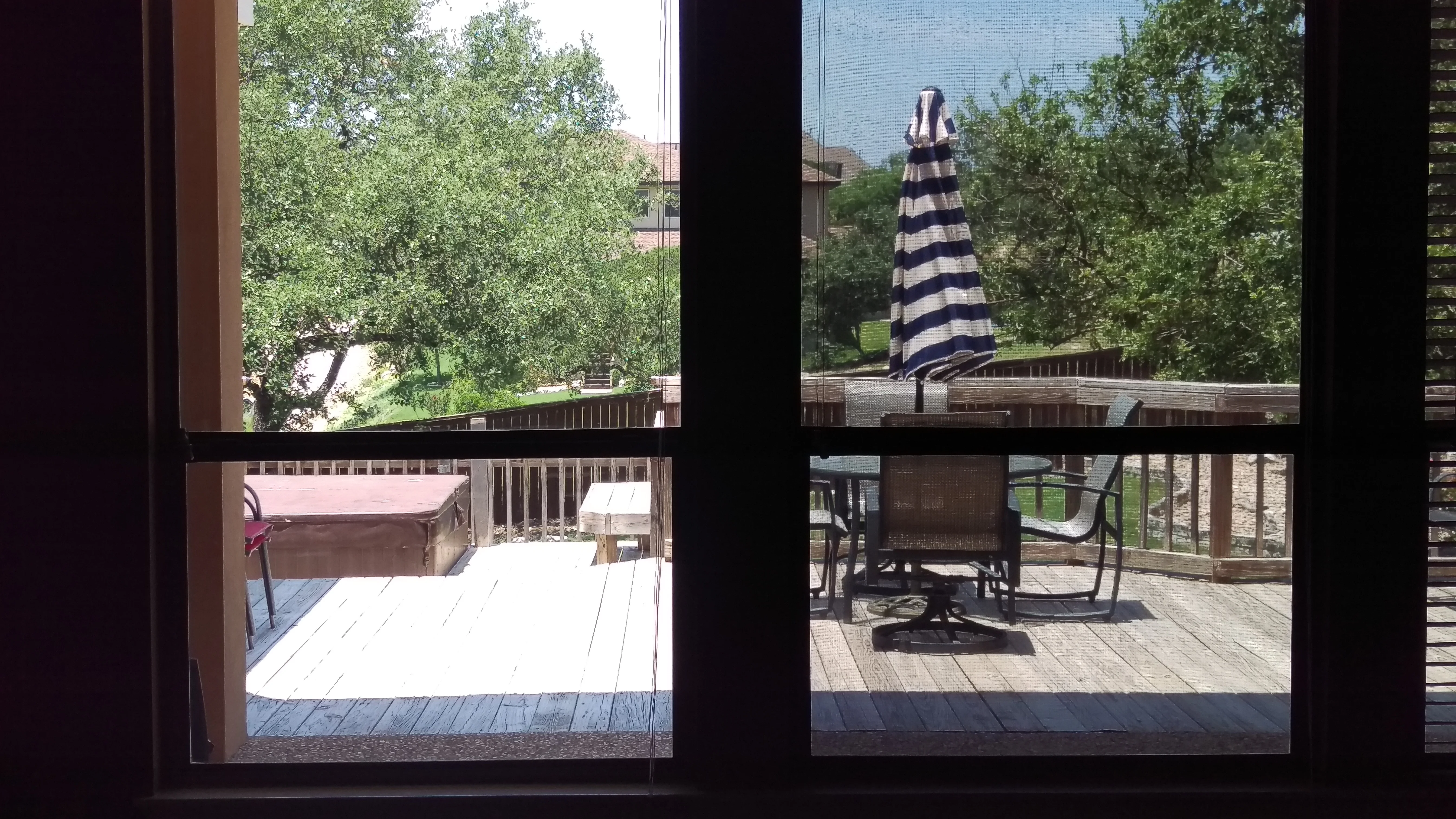 Solar shade screens installed on multi-panel glass doors and windows overlooking deck with striped umbrella and furniture