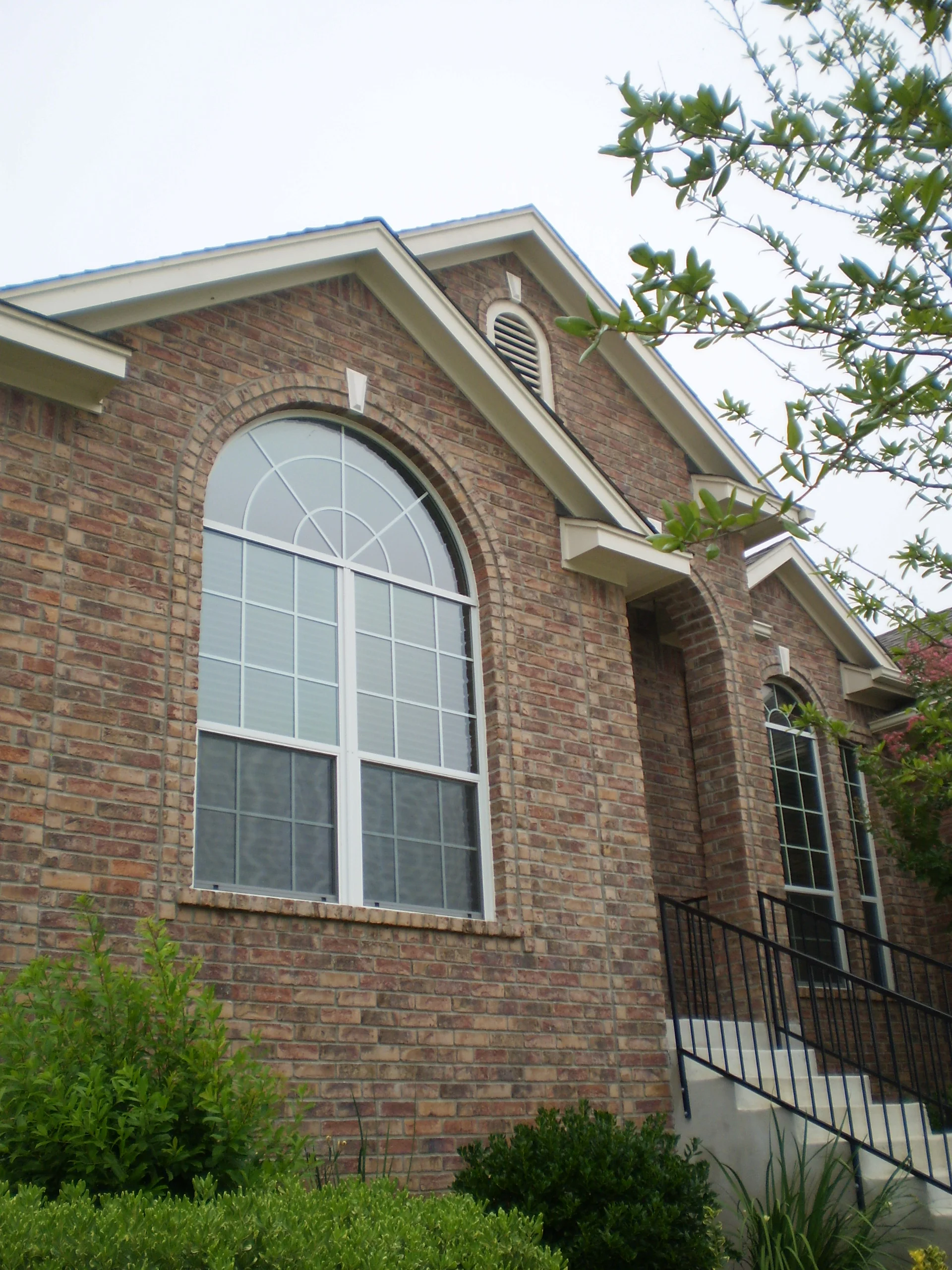 Large arched window with white frame and gridded panes installed in brick exterior wall