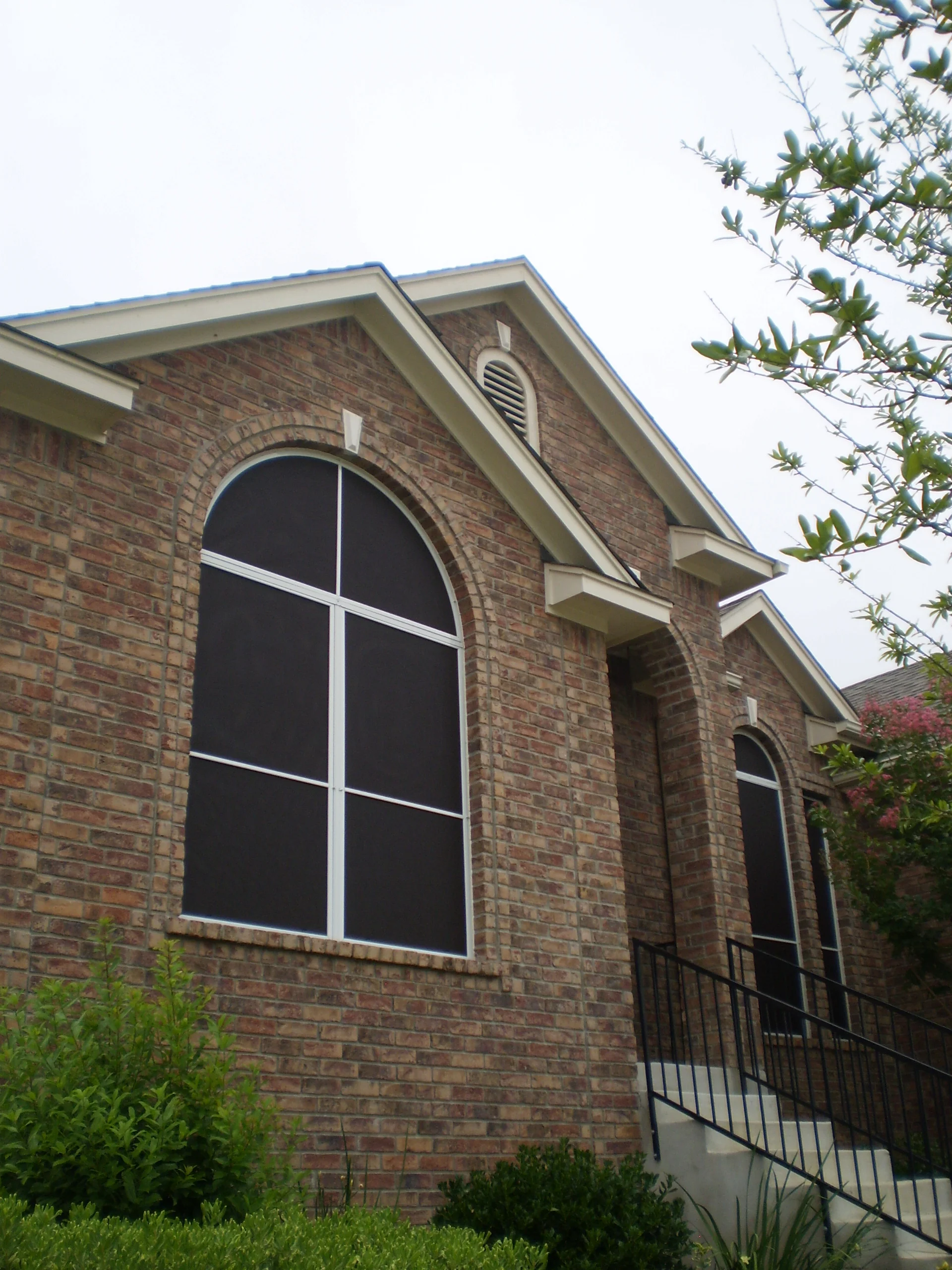 Arched and rectangular windows with white-framed solar screens on brick exterior