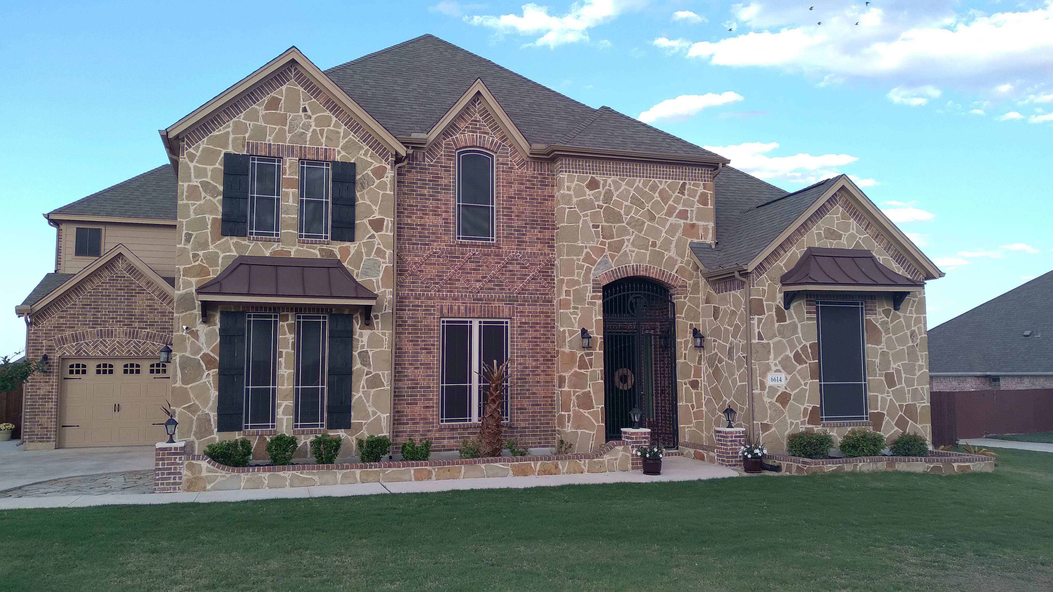 Stone and brick home with black-framed windows and glass doors installed on front facade
