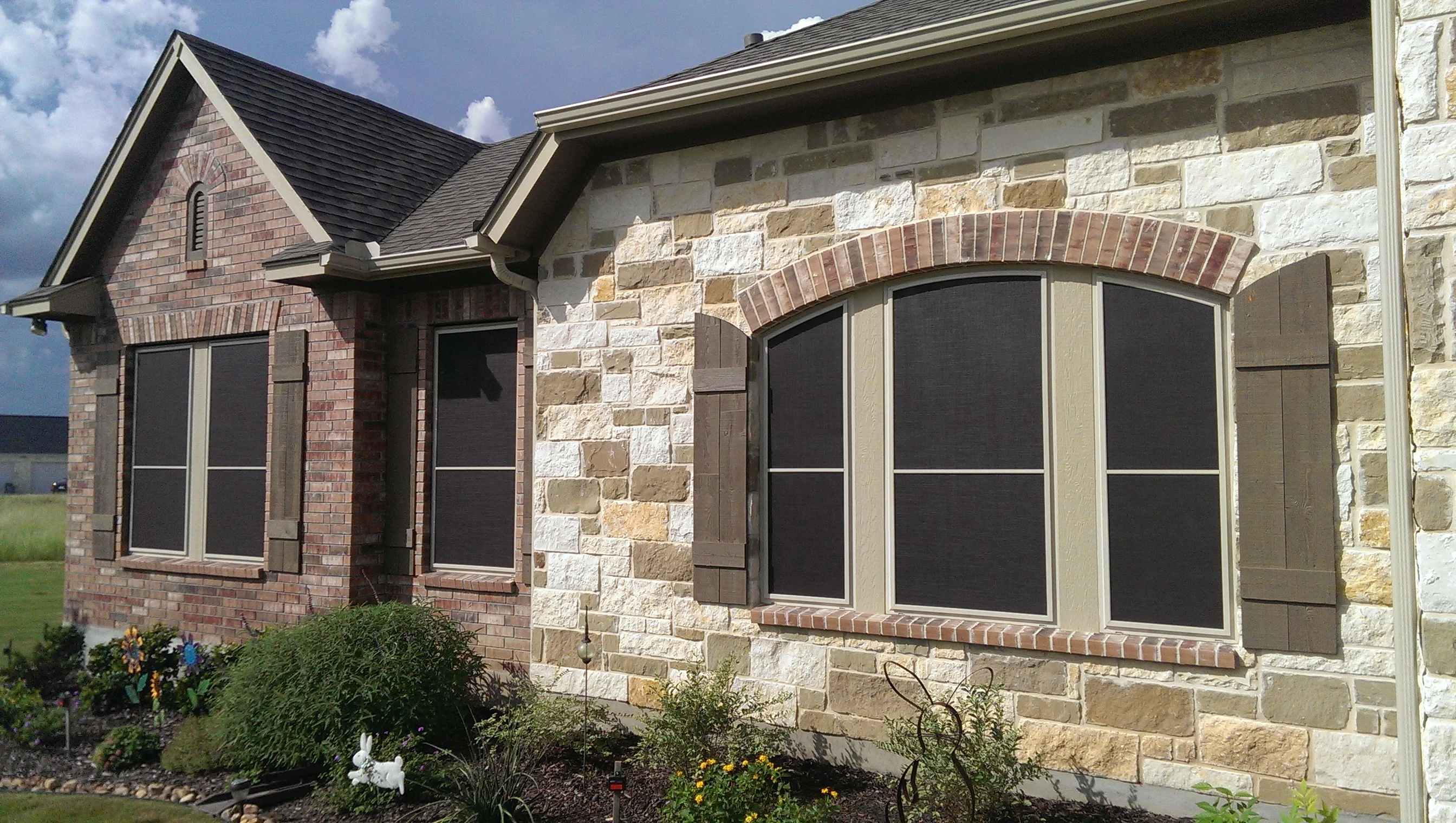 Three large windows with dark solar screens installed on stone and brick home exterior with arched brick detailing