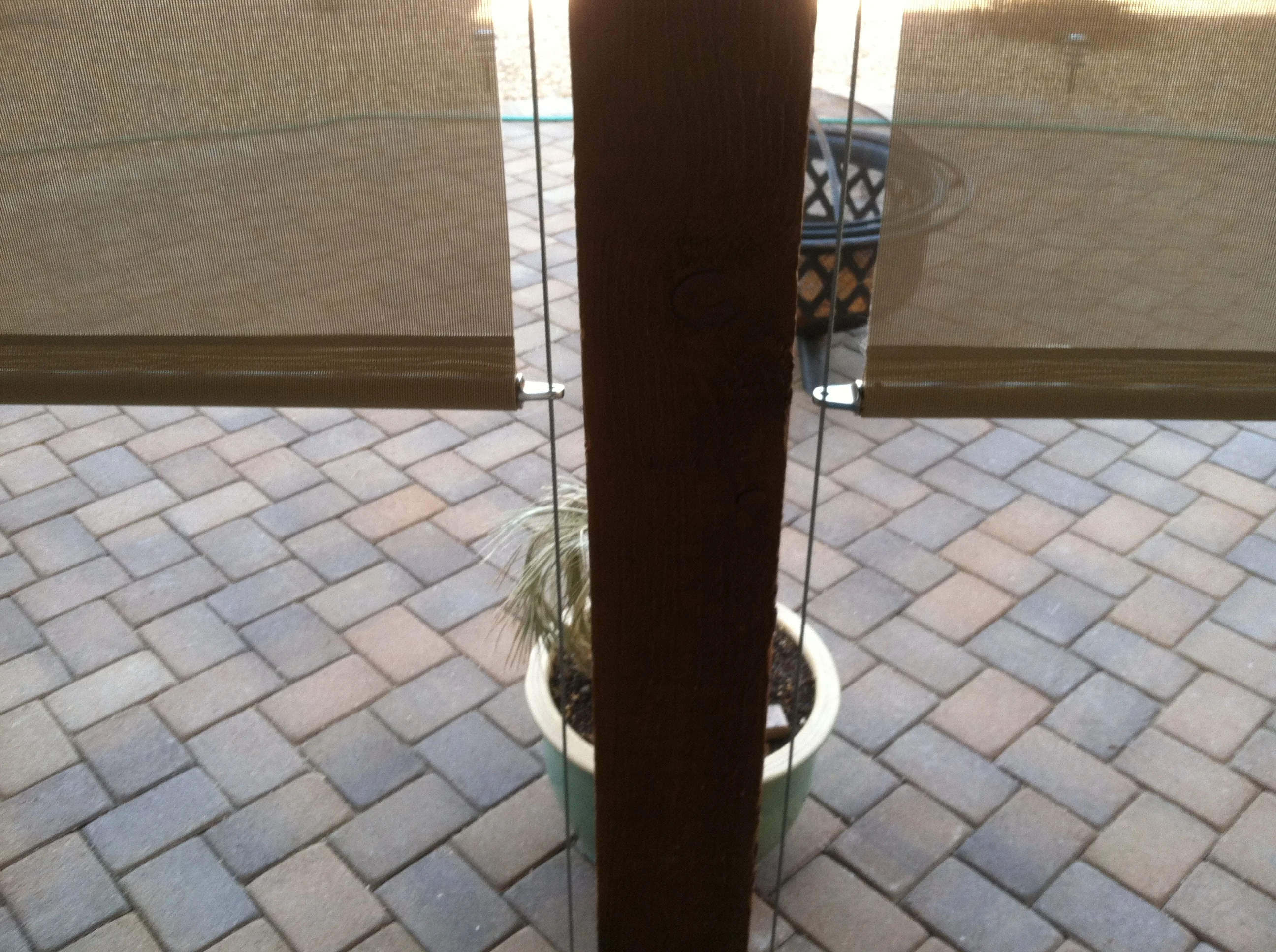 Dark brown retractable solar screen with cable system mounted between glass panels on paver patio