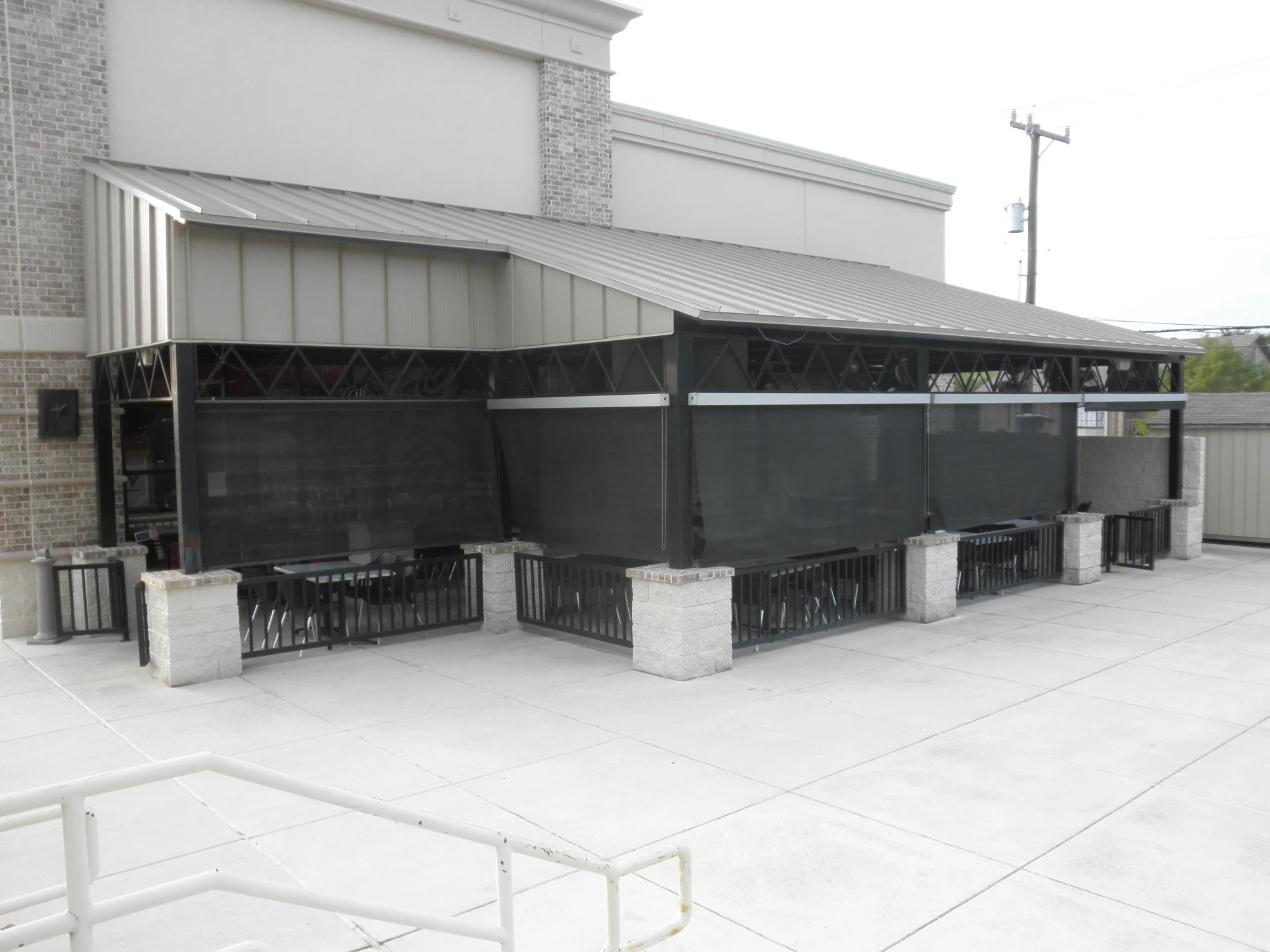 Metal patio structure with black solar shade screens, metal railings, and sloped metal roof